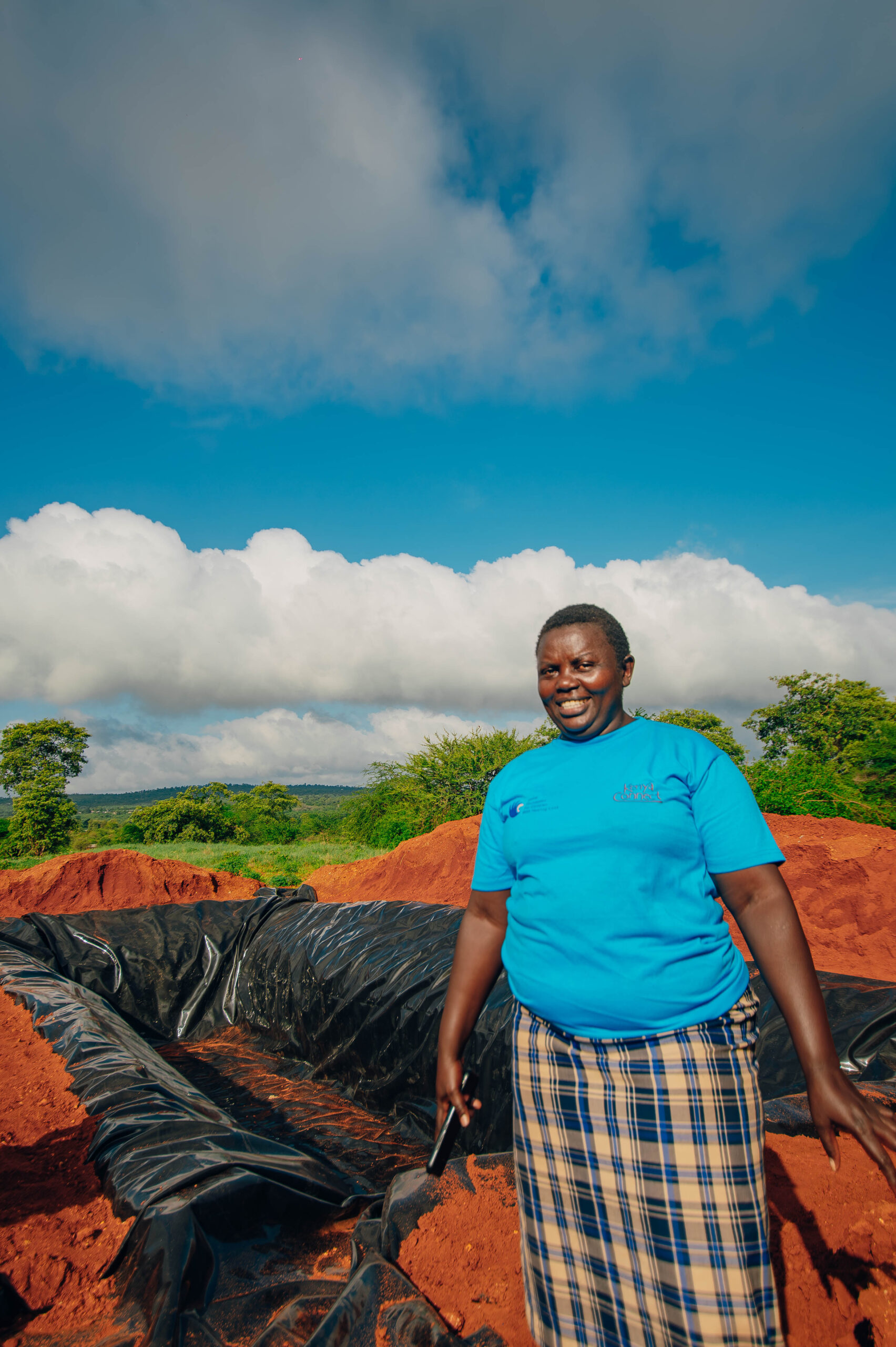 Pauline, a smallholder farmer in Machakos standing next to a water pan built for her by IAG.