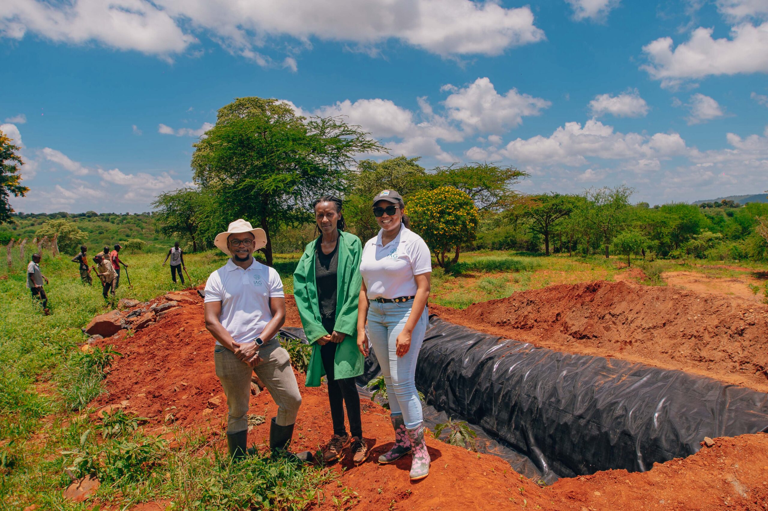 IAG founders standing alongside Wendy (middle) next to the water pan we are building in her farm.